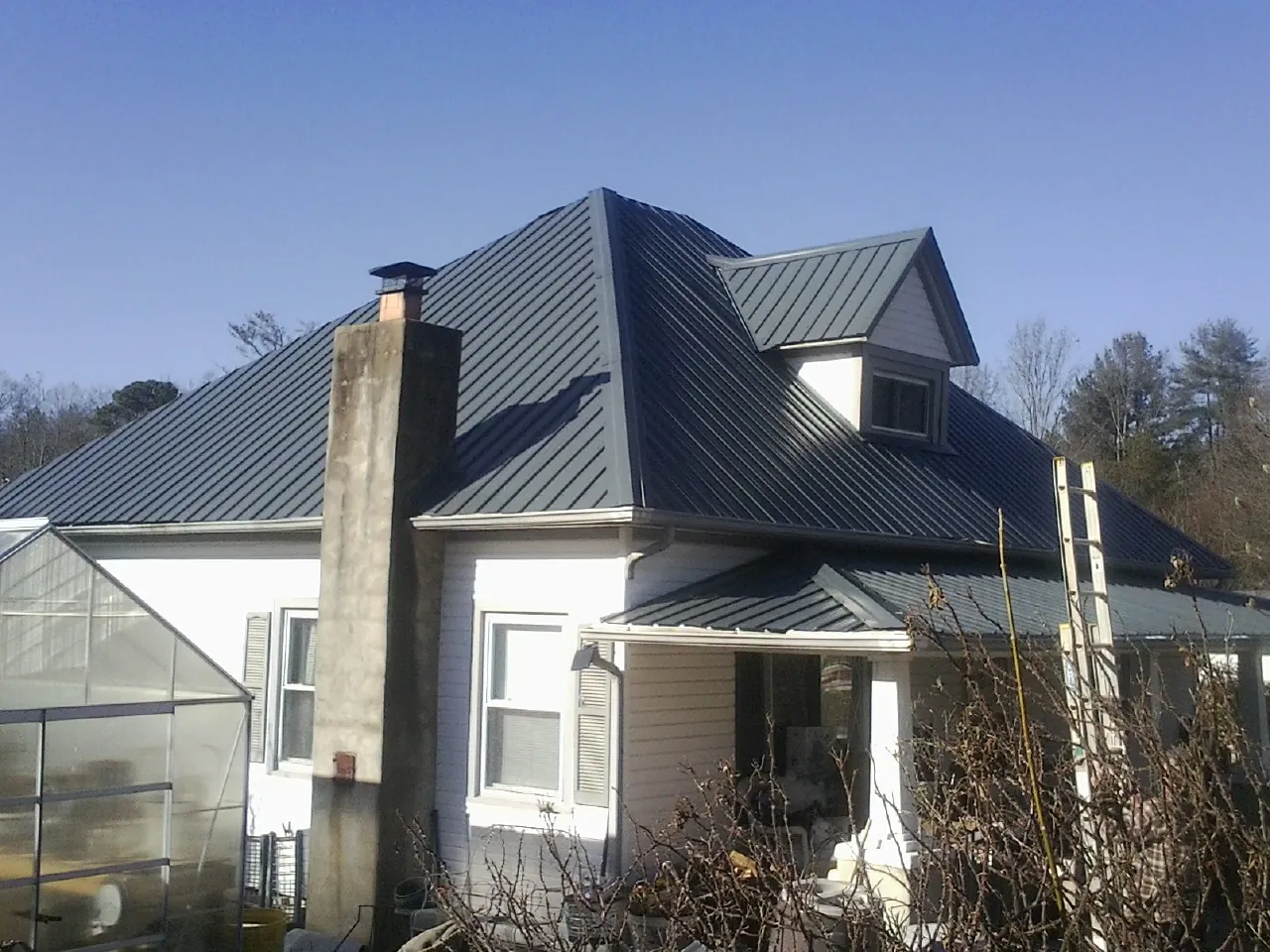 Dark blue standing seam metal roof on a white farmhouse with dormer — Slate & Tile Roof Repair by Roofing Brothers in Metropolis