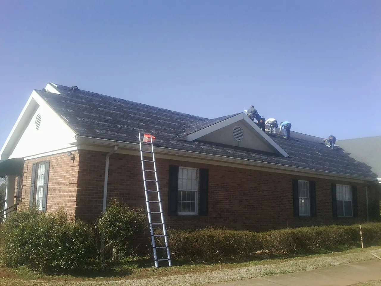 Crew tearing shingles off a brick ranch roof with a ladder set — Metal Roof Repair work by our crew in Metropolis