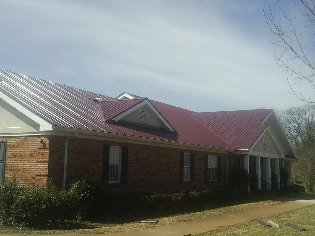 Red metal roof with gabled entries on a long brick building, from a Hail Damage Roof Repair job in Metropolis