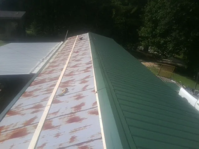 Old rusted panels beside newly installed green metal roofing — Wind Damage Roof Repair by Roofing Brothers in Metropolis