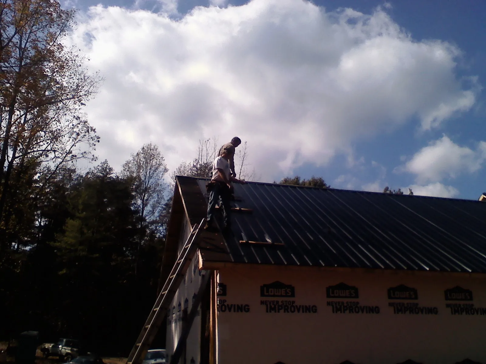 Roofer fastening dark metal panels high against a cloudy sky, from a Roof Inspection job in Metropolis
