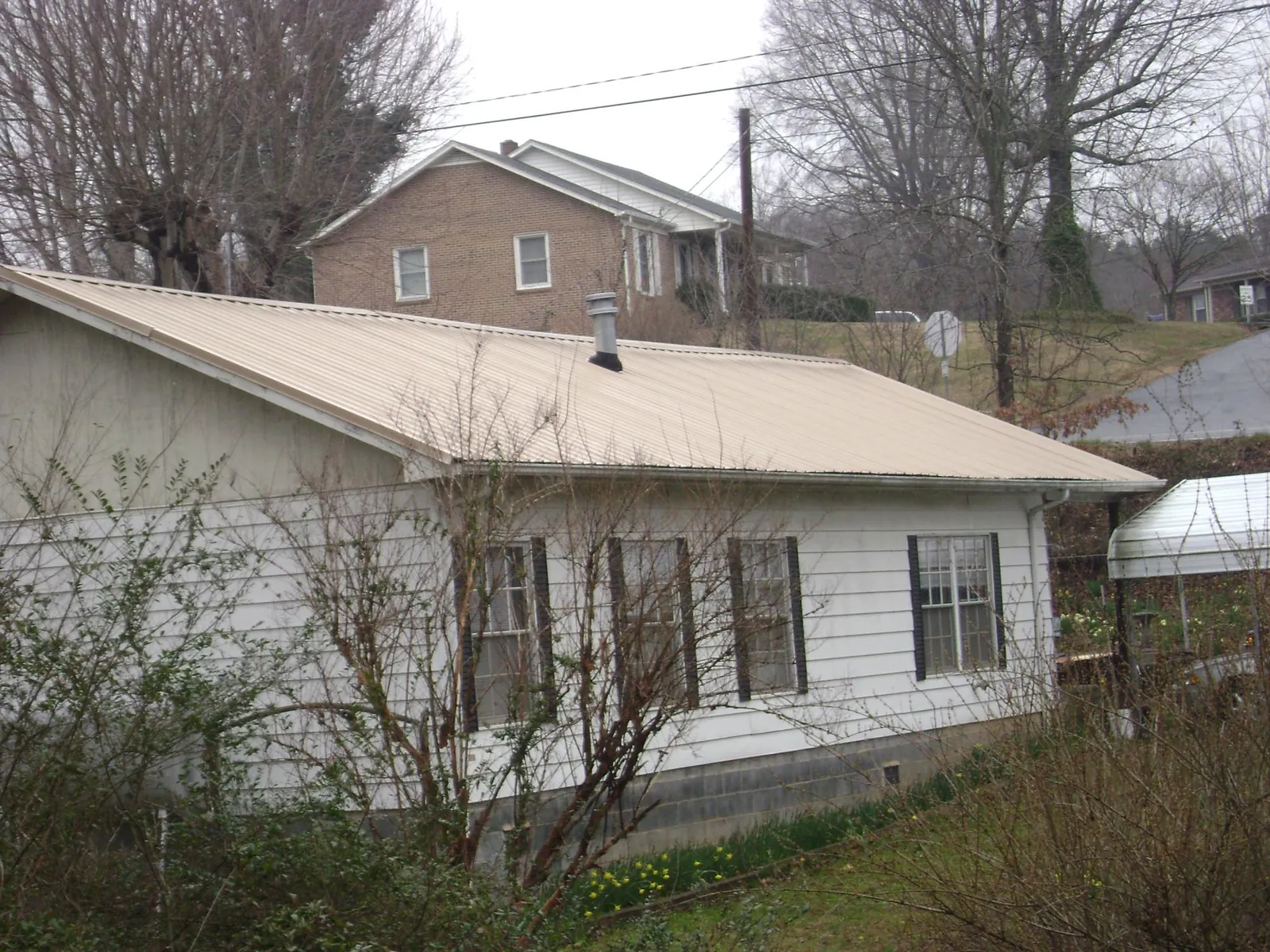 Tan metal roof on a white sided house set into a hillside — Commercial Roofing by Roofing Brothers in Metropolis