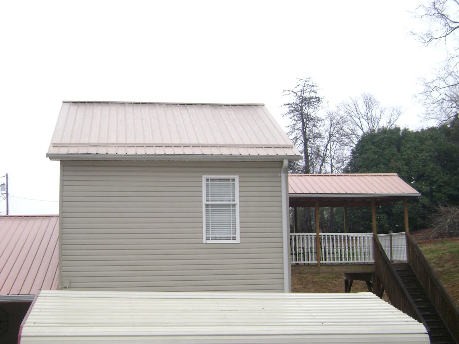 Tan metal roofs on a two story addition and attached porch, from a Roof Replacement job in Metropolis
